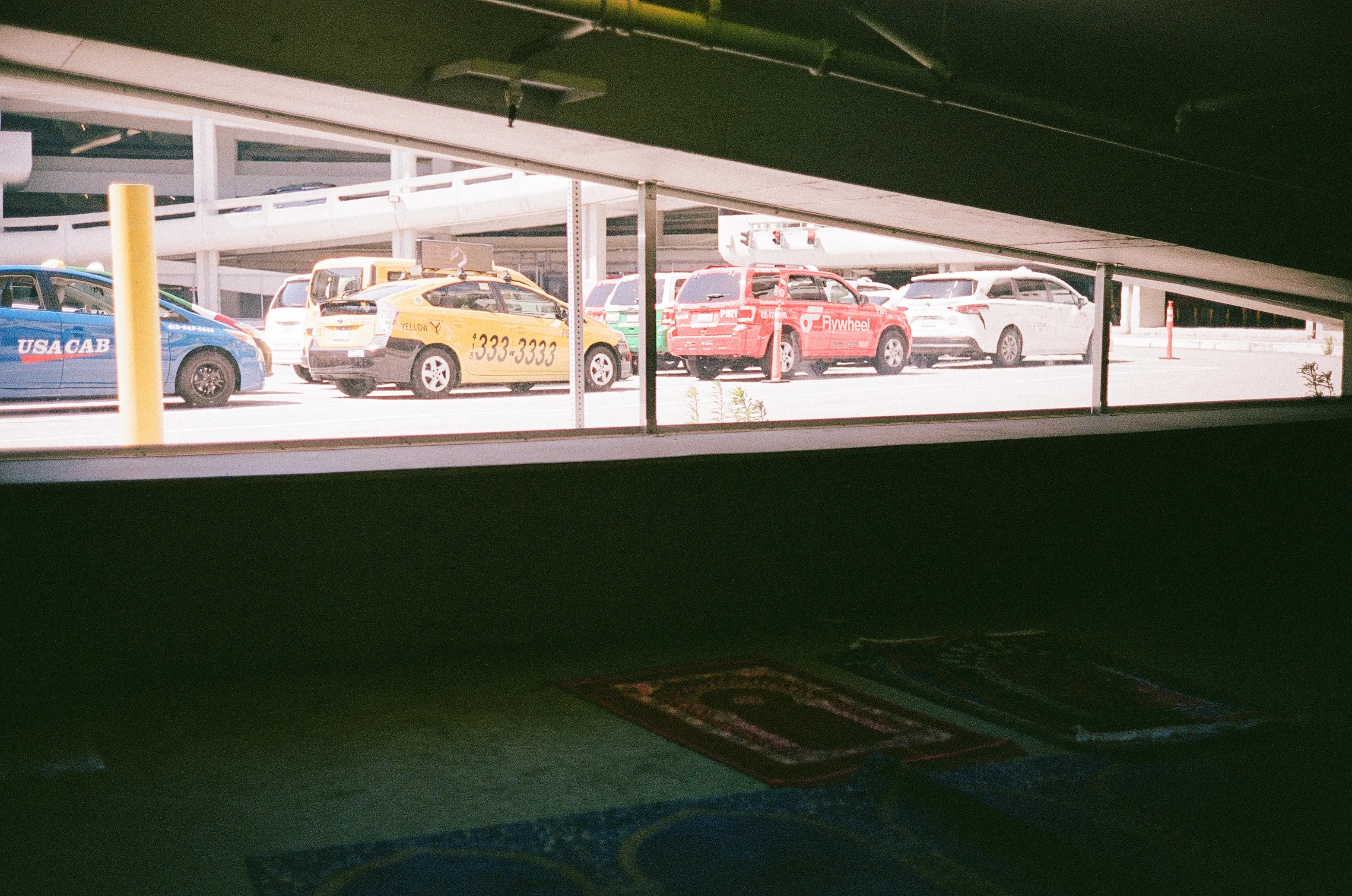 Within the prayer hall; prayer rugs in foreground with taxis waiting in queue behind a wind shield